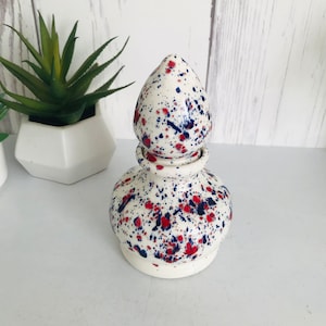 Op de afbeelding: Witte keramische flessenstop met een splatterpatroon van rode, blauwe en witte verf.