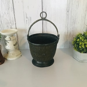 Peut inclure: Un petit seau en métal vert foncé avec une texture martelée et une poignée en métal noir. Le seau a une forme ronde et un bord légèrement évasé.