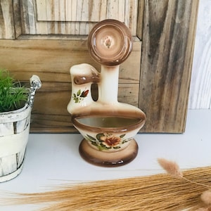 Könnte beinhalten: Ein Keramik-Pflanztopf in Form eines Vintage-Waschbeckens mit brauner und weißer Glasur. Der Topf ist mit floralen Mustern in Braun-, Orange- und Weißtönen verziert.