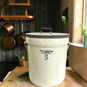 Peut inclure: Un pot en céramique de couleur crème avec un couvercle en bois foncé et une poignée en métal. L'avant présente un texte noir indiquant Alberta Potteries Ltd. Medicine Hat Alta et un grand chiffre 5. Le récipient cylindrique a deux anses latérales.