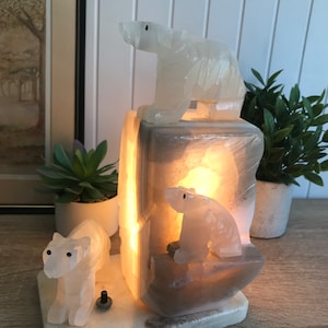 May include: A white alabaster lamp with three polar bear sculptures. The lamp is lit and the light shines through the alabaster.