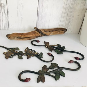 Può includere: Tre ganci in metallo decorativi con un design floreale e farfalla. I ganci sono dipinti in tonalità di verde, marrone e rosso.