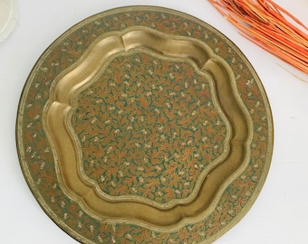 May include: A round brass serving tray with a decorative design of green and orange floral patterns. The tray has a raised rim and a scalloped edge.