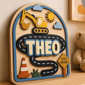Può includere: Decorazione murale in legno a tema costruzione con il nome "THEO". Il design include un escavatore giallo, una strada, un sole, nuvole e un cartello "Little Builder". L'opera è incorniciata in blu. Misure in centimetri.