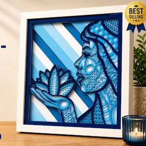 May include: A laser-cut multilayer shadow box featuring a woman and lotus design. The artwork is predominantly blue, with a white frame. The text "Woman-Lotus" is displayed prominently. The design is suitable for mandala decor.