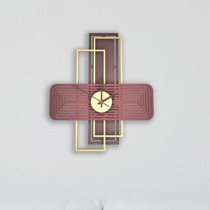 Op de afbeelding: Een witte bank met twee witte kussens en een geometrische wandklok met een gouden frame en een bordeauxrode wijzerplaat. De klok hangt aan een witte muur.