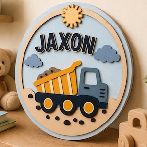 Può includere: Un cartello rotondo in legno con il nome "Jaxon" in lettere blu scuro. Il cartello presenta uno sfondo azzurro con un sole giallo, nuvole blu e un camion ribaltabile. Il camion ribaltabile è giallo e blu, con terra marrone nel cassone.