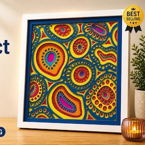 Puede incluir: Una caja de sombra abstracta multicapa enmarcada con un diseño de mandala vibrante. La obra de arte presenta una combinación de colores amarillo, naranja, rosa y azul. El marco es blanco con un borde azul. El texto en la imagen incluye "Laser Cut Abstract" y "Mandala Decor."