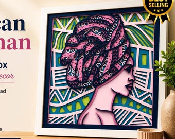 Peut inclure: Boîte à ombre multicouche représentant une femme africaine avec un turban rose à motifs. L'œuvre est encadrée en blanc avec un bord bleu marine, avec des motifs géométriques verts et bleus en arrière-plan. Le texte "African Woman" est affiché en haut.
