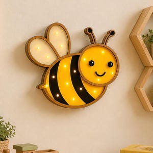 May include: A wooden bee-shaped wall light with a smiling face, black stripes, and glowing lights. The image also shows a teddy bear, a wooden train, and a framed picture of a beehive. The text "INSTANT DOWNLOAD" is visible.