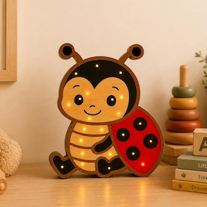 May include: A wooden ladybug-shaped night light with a smiling face and glowing lights. The ladybug has a red wing with black dots. The image also includes a teddy bear, a wooden car, and a stack of children's books.