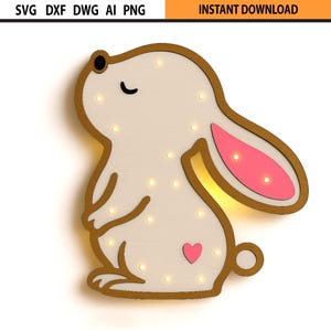 Puede incluir: Una luz en forma de conejito de madera con cuerpo crema, contorno dorado y detalles rosas en las orejas y un corazón. El conejito tiene pequeñas luces y el texto "INSTANT DOWNLOAD" está en la esquina superior derecha.