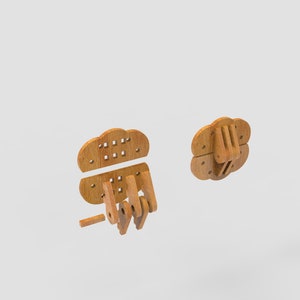 May include: Wooden puzzle pieces in the shape of a hand, with a cloud-like top. The pieces are light brown and appear to be unassembled. The design includes a fist and a separate cloud-shaped piece with small square holes.