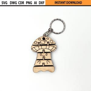 May include: A wooden mushroom-shaped keychain with a silver keyring. The mushroom has a smiling face and is made of interlocking pieces. The top of the image has the text "SVG DWG CDR PNG AI DXF" and "INSTANT DOWNLOAD".