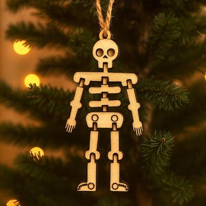 May include: A wooden skeleton ornament hangs from a twine string against a backdrop of a Christmas tree. The skeleton has articulated joints and a skull-shaped head. The ornament is made of light-colored wood and is a festive decoration.