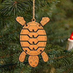 May include: A wooden turtle Christmas ornament with a natural wood finish hangs from a twine string. The ornament is laser-cut with detailed segments and circular patterns. A red Christmas light is visible in the background.