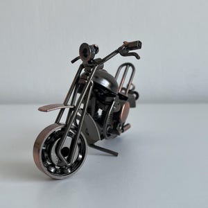 May include: A small, metal motorcycle sculpture with a black and copper finish. The motorcycle is made of various metal pieces, including nuts, bolts, and washers.