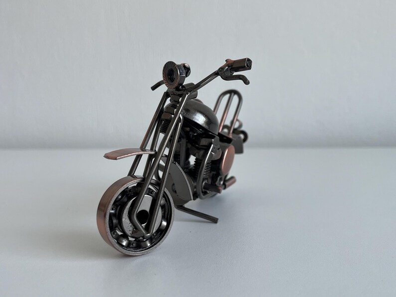 May include: A small, metal motorcycle sculpture with a black and copper finish. The motorcycle is made of various metal pieces, including nuts, bolts, and washers.