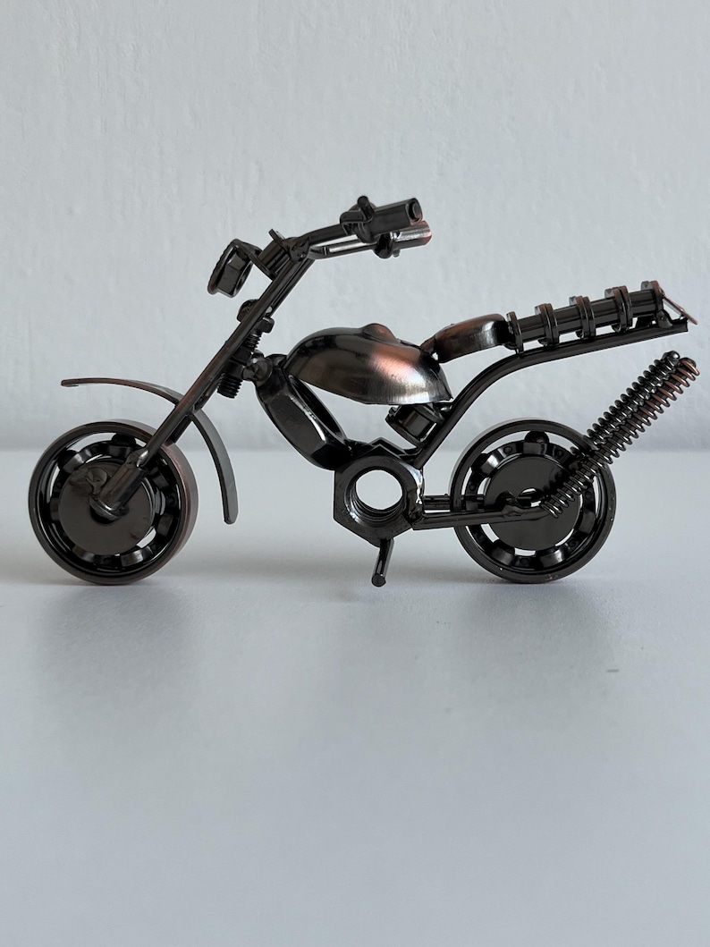 May include: A small, metal motorcycle sculpture made from nuts, bolts, and other hardware. The motorcycle is painted a dark bronze color and has a detailed design.
