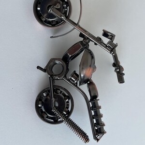 May include: A small, metal motorcycle sculpture made from nuts, bolts, and other hardware. The motorcycle is in a wheelie position with the front wheel in the air. The sculpture is painted in a dark metallic color.