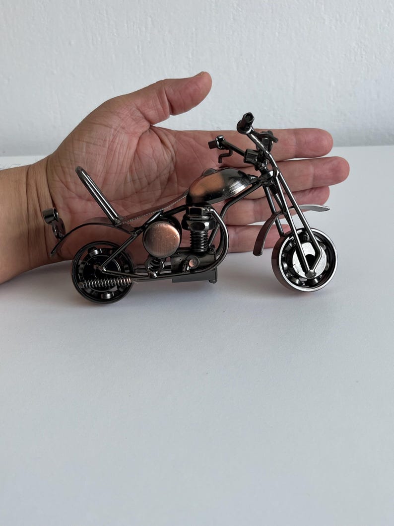 May include: A small, metal motorcycle figurine with a copper-colored gas tank and black metal accents. The motorcycle is on a white surface.