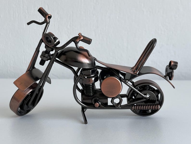 May include: A small, metal motorcycle sculpture made of nuts, bolts, and other metal pieces. The motorcycle is painted in a dark bronze color.