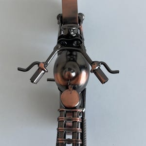 May include: A small metal motorcycle sculpture with a copper finish. The motorcycle is made of recycled metal and has a unique, handcrafted look.
