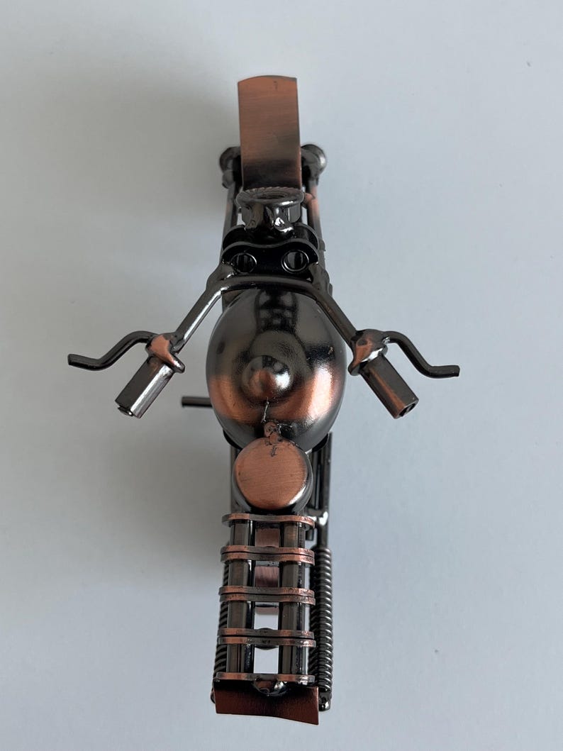May include: A small metal motorcycle sculpture with a copper finish. The motorcycle is made of recycled metal and has a unique, handcrafted look.