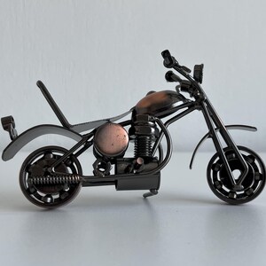 May include: A black metal motorcycle sculpture with a copper-colored engine and wheels. The motorcycle is made of recycled metal parts and is a unique and decorative piece.