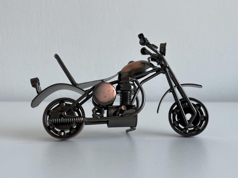 May include: A black metal motorcycle sculpture with a copper-colored engine and wheels. The motorcycle is made of recycled metal parts and is a unique and decorative piece.