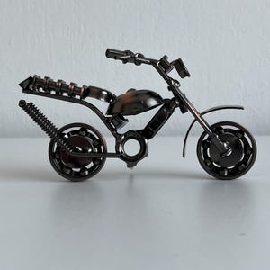 May include: A small, black metal motorcycle sculpture made from nuts, bolts, and other metal pieces. The motorcycle has a detailed design and is a unique piece of art.