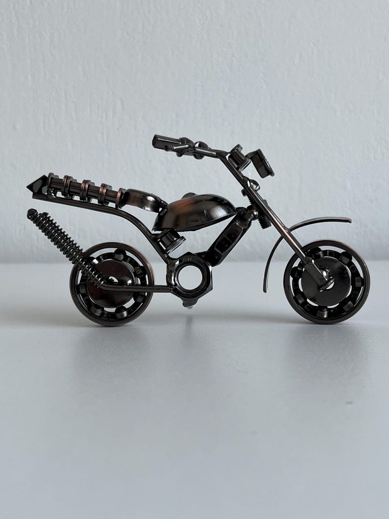 May include: A small, black metal motorcycle sculpture made from nuts, bolts, and other metal pieces. The motorcycle has a detailed design and is a unique piece of art.