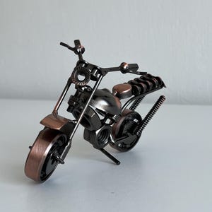 May include: A small, metal motorcycle sculpture made of nuts, bolts, and other hardware. The motorcycle is black with copper accents.