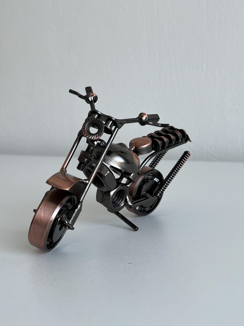 May include: A small, metal motorcycle sculpture made of nuts, bolts, and other hardware. The motorcycle is black with copper accents.