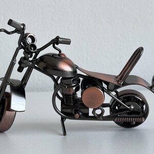 May include: A small, metal motorcycle figurine with a copper finish. The motorcycle has a detailed engine and wheels, and a small seat.