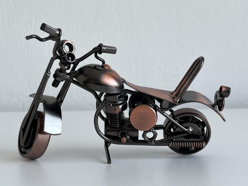 May include: A small, metal motorcycle figurine with a copper finish. The motorcycle has a detailed engine and wheels, and a small seat.