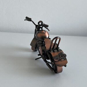 May include: A small, metal motorcycle figurine with a copper finish. The motorcycle has a black seat and handlebars.