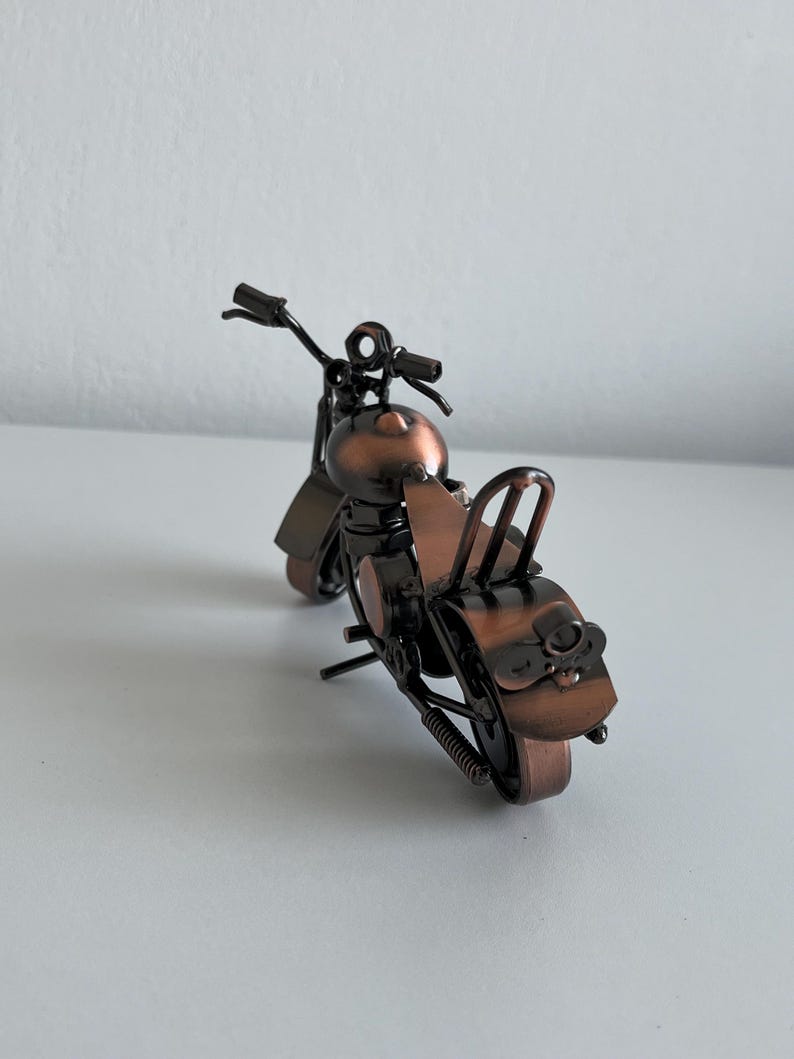 May include: A small, metal motorcycle figurine with a copper finish. The motorcycle has a black seat and handlebars.