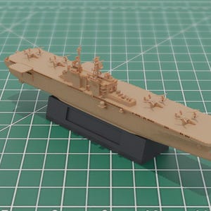 May include: A tan model aircraft carrier with miniature aeroplanes on the deck, mounted on a black base. The model is set against a green grid background. The model is a detailed replica.