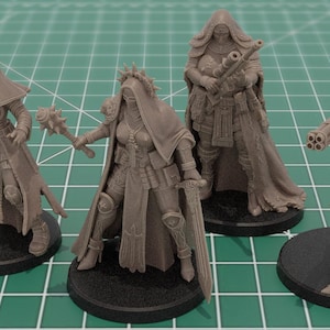Op de afbeelding: Vier onbeschilderde grijze hars miniatuurfiguren op zwarte ronde voetstukken. Elk figuur draagt een kapmantel en tactische uitrusting. De figuren zijn uitgerust met diverse wapens, waaronder een pistool, een strijdhamer, een geweer en een vuurwapen.