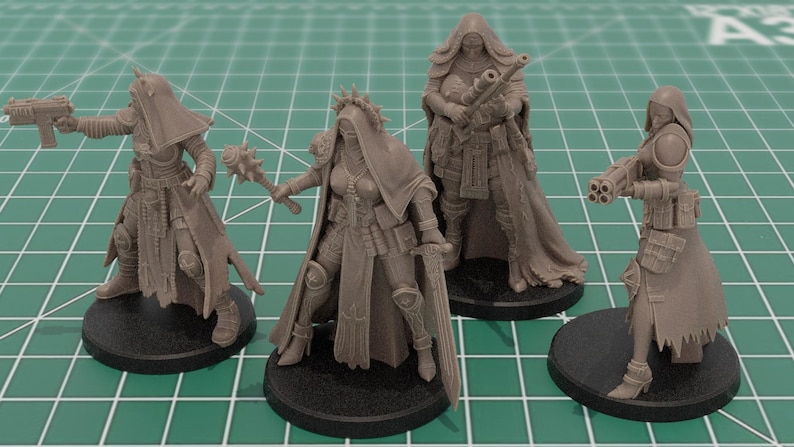Op de afbeelding: Vier onbeschilderde grijze hars miniatuurfiguren op zwarte ronde voetstukken. Elk figuur draagt een kapmantel en tactische uitrusting. De figuren zijn uitgerust met diverse wapens, waaronder een pistool, een strijdhamer, een geweer en een vuurwapen.