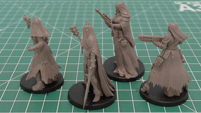 Op de afbeelding: Vier ongeverfde grijze hars miniatuurfiguren op ronde zwarte voetstukken. Elk figuur draagt een kapmantel en tactische uitrusting. De figuren zijn uitgerust met diverse wapens, waaronder een pistool, een strijdhamer, een geweer en een zwaar vuurwapen.