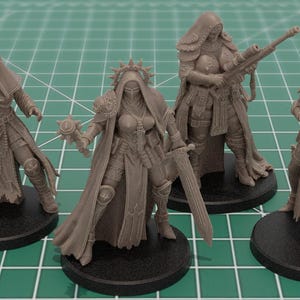 Op de afbeelding: Een set van vier ongeverfde grijze hars miniatuurfiguren op ronde zwarte voetstukken. Elk figuur stelt een krijger voor in een gewaad met capuchon en harnas, uitgerust met diverse wapens waaronder een pistool, een zwaard, een geweer en een meervoudig loopwapen.