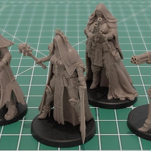 Op de afbeelding: Vier ongeverfde grijze hars tabletop spelminiaturen op ronde zwarte voetstukken. De figuren dragen capuchonmantels en tactische uitrusting en houden verschillende wapens vast, waaronder een pistool, een strijdvlegel, een geweer en een wapen met meerdere lopen.