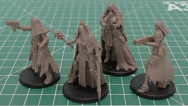 Op de afbeelding: Vier ongeverfde grijze hars tabletop spelminiaturen op ronde zwarte voetstukken. De figuren dragen capuchonmantels en tactische uitrusting en houden verschillende wapens vast, waaronder een pistool, een strijdvlegel, een geweer en een wapen met meerdere lopen.