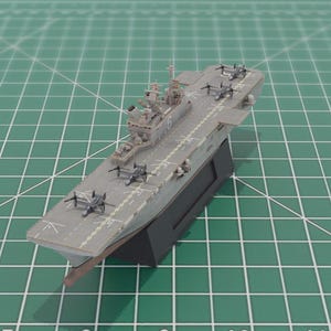 May include: A detailed model of a grey aircraft carrier with miniature aeroplanes on the deck. The model is mounted on a black base against a green grid background. The carrier features intricate details.