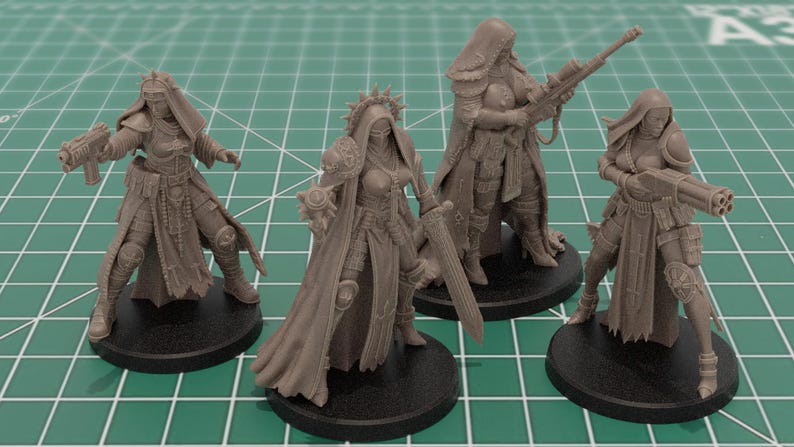 Op de afbeelding: Vier onbeschilderde miniatuurfiguren van grijze hars op ronde zwarte voetstukken. Elk figuur draagt een harnas met capuchon en draagt een ander wapen, waaronder een pistool, een zwaard, een sluipschuttersgeweer en een zwaar wapen met meerdere lopen.