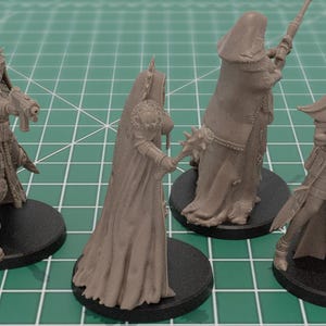 Op de afbeelding: Vier ongeverfde lichtbruine hars miniatuurfiguren op ronde zwarte voetstukken. De figuren tonen gepantserde personages in lange gewaden, sommigen houden geweren vast en &eacute;&eacute;n houdt een knots met stekels, allemaal met gedetailleerde tactische uitrusting.