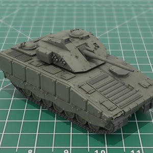 May include: A detailed model of a military tank in a muted green color. The tank features a long barrel, multiple turrets, and intricate detailing on its exterior. It sits on a green grid surface, suggesting a scale model or hobbyist project.