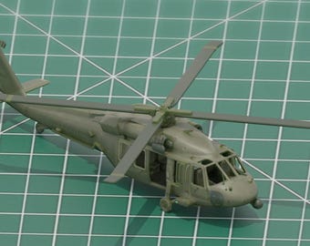 May include: A scale model of a military helicopter in olive drab green. The aircraft features a main rotor with four blades, a tail rotor, a cockpit with clear windows, and landing gear. The fuselage includes side doors and a tapered tail section.